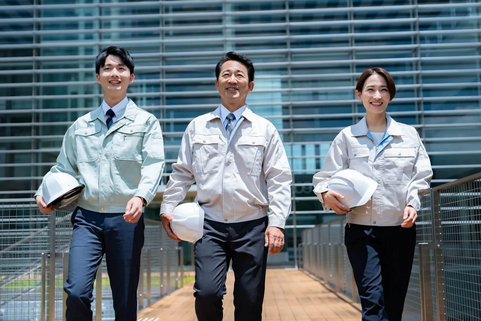 ヘルメットを持って笑顔で歩く3人の会社員