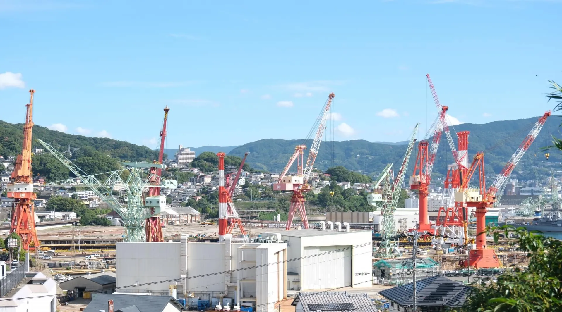 複数の赤白および緑色の大型クレーンが稼働する造船所の工事現場