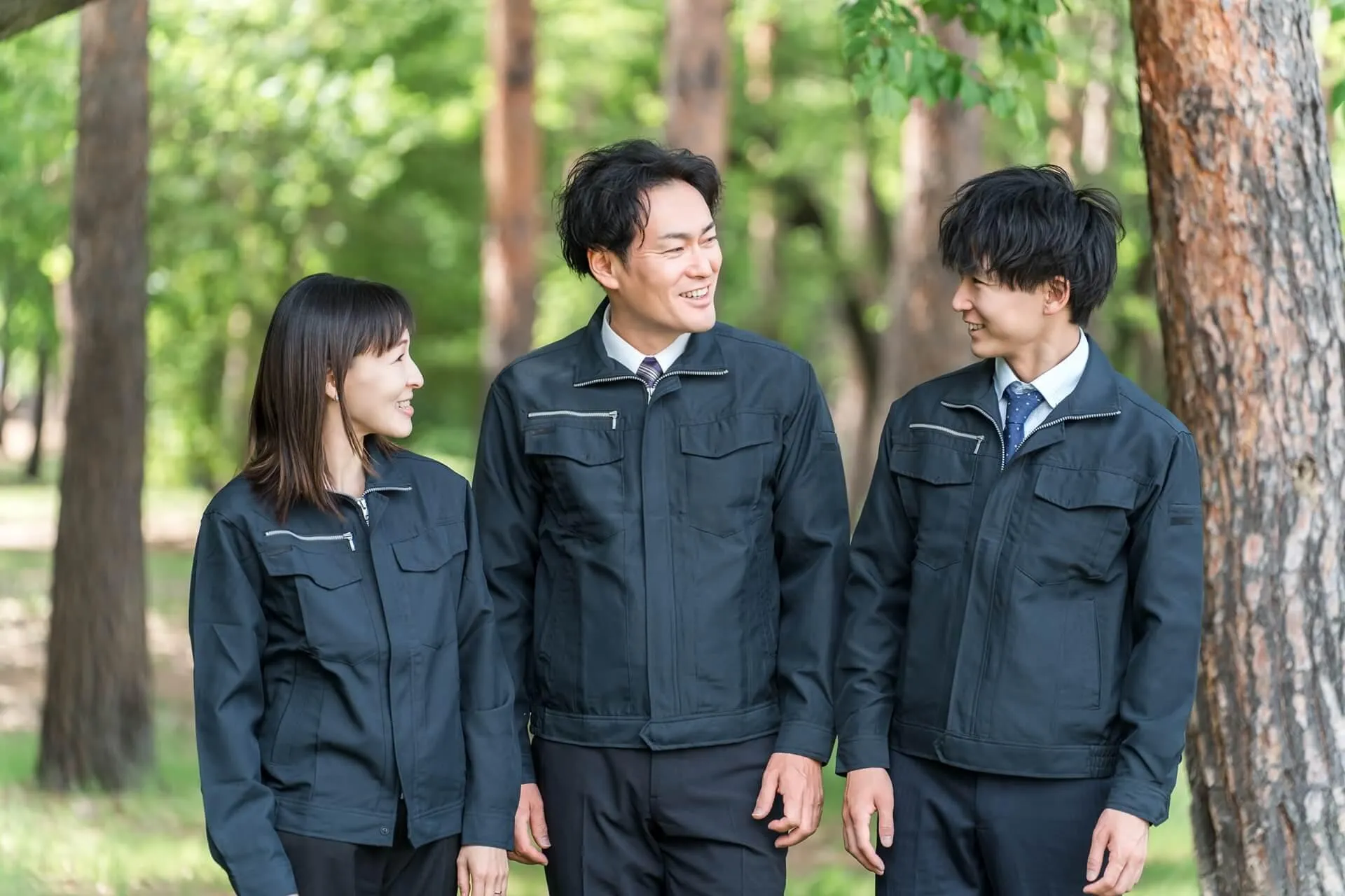 森の中で喋る黒い作業服を着た3人の建設会社のスッタッフ